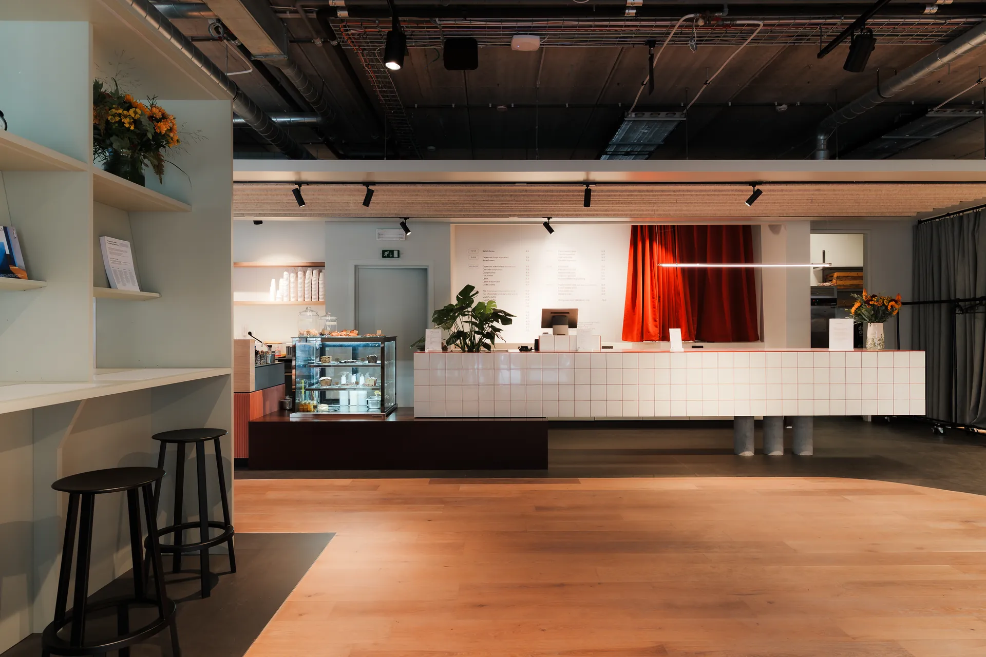 The counter at Bump's Café Concept — a long white tiled bar with open shelving, a pastry case and a red curtain behind