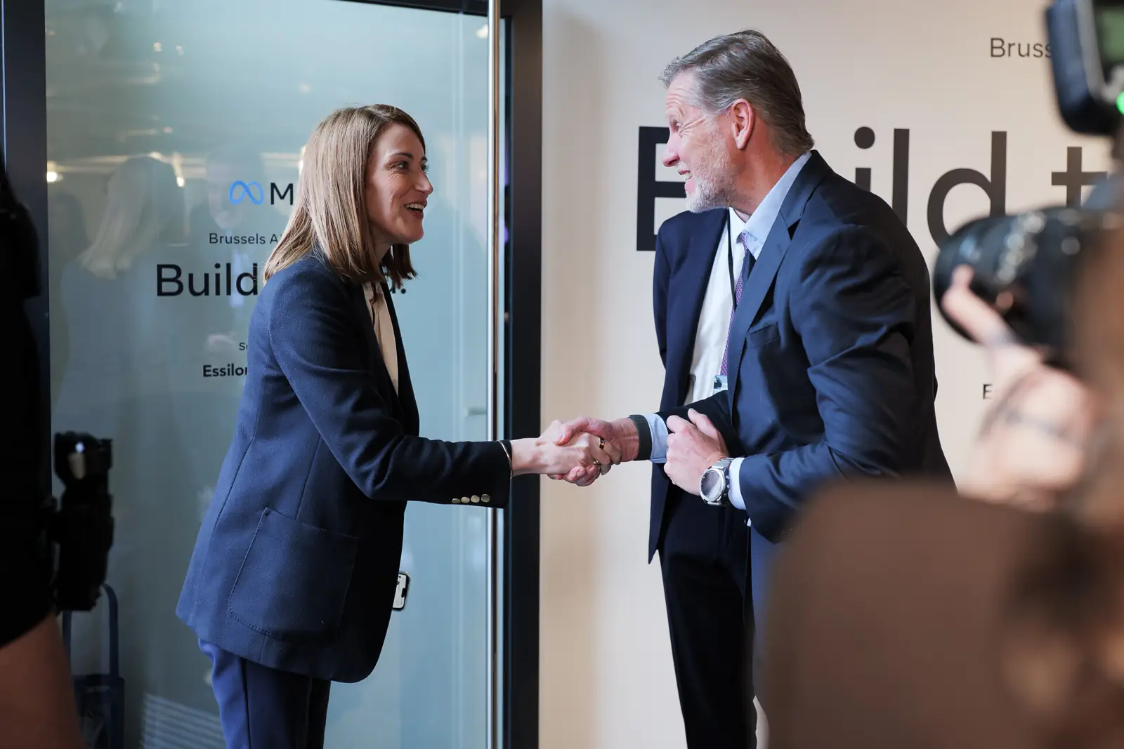 Two guests shaking hands in front of the &ldquo;Build to lead.&rdquo; wall