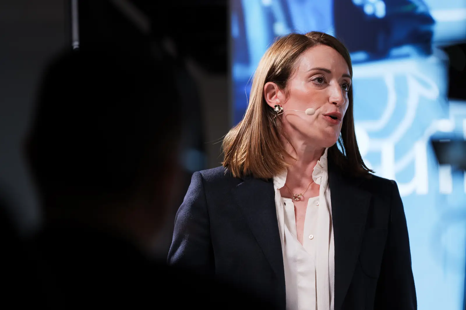 A keynote speaker on stage, lit by the screen behind