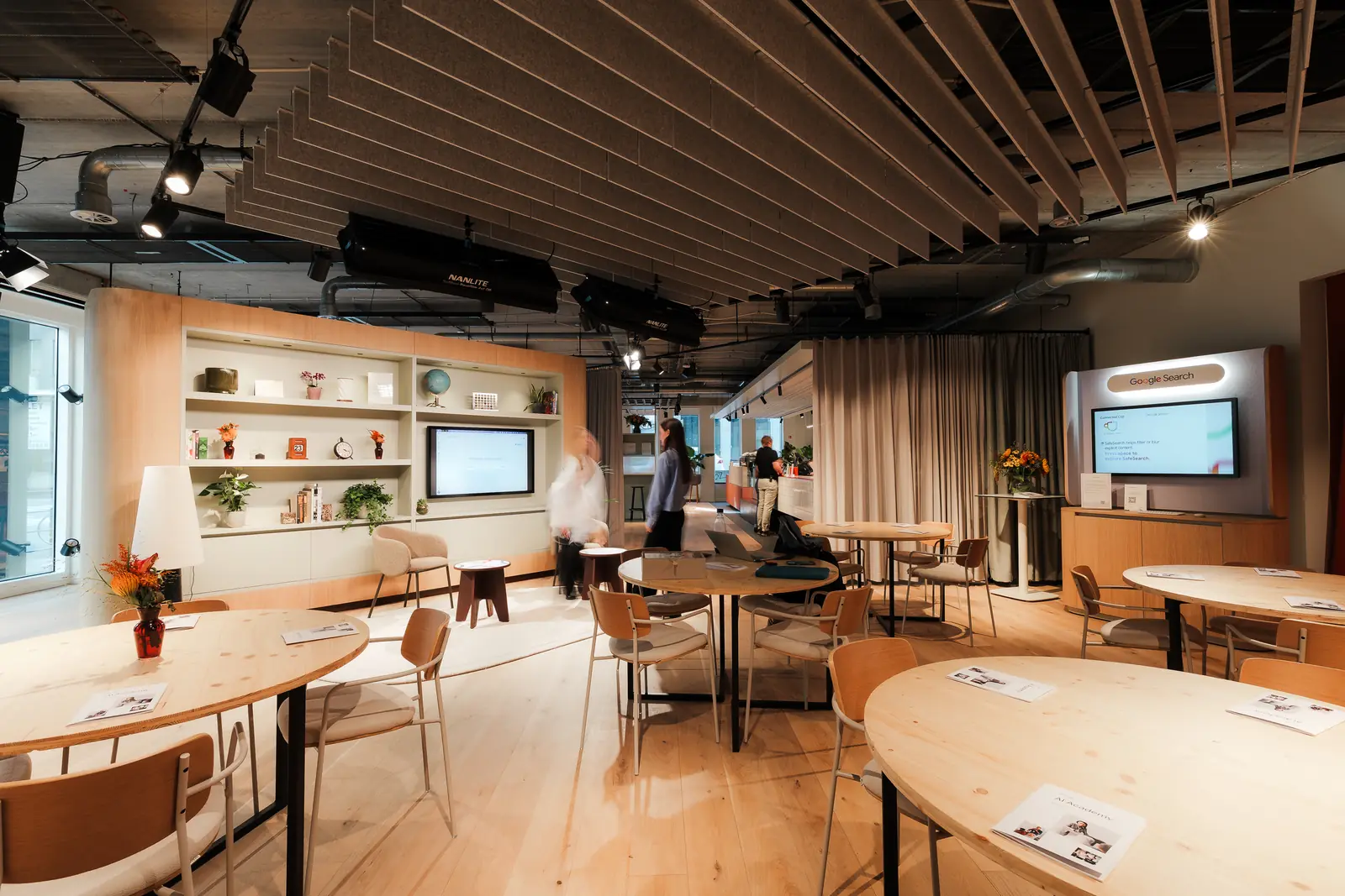 The room set with round tables for a session, guests standing by the shelving and screen