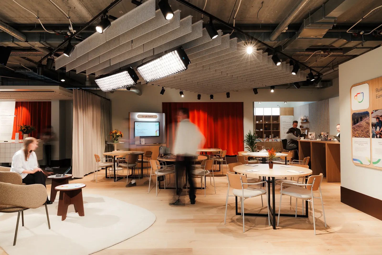 The pop-up in use during the day, round tables and lounge seating under a lighting rig