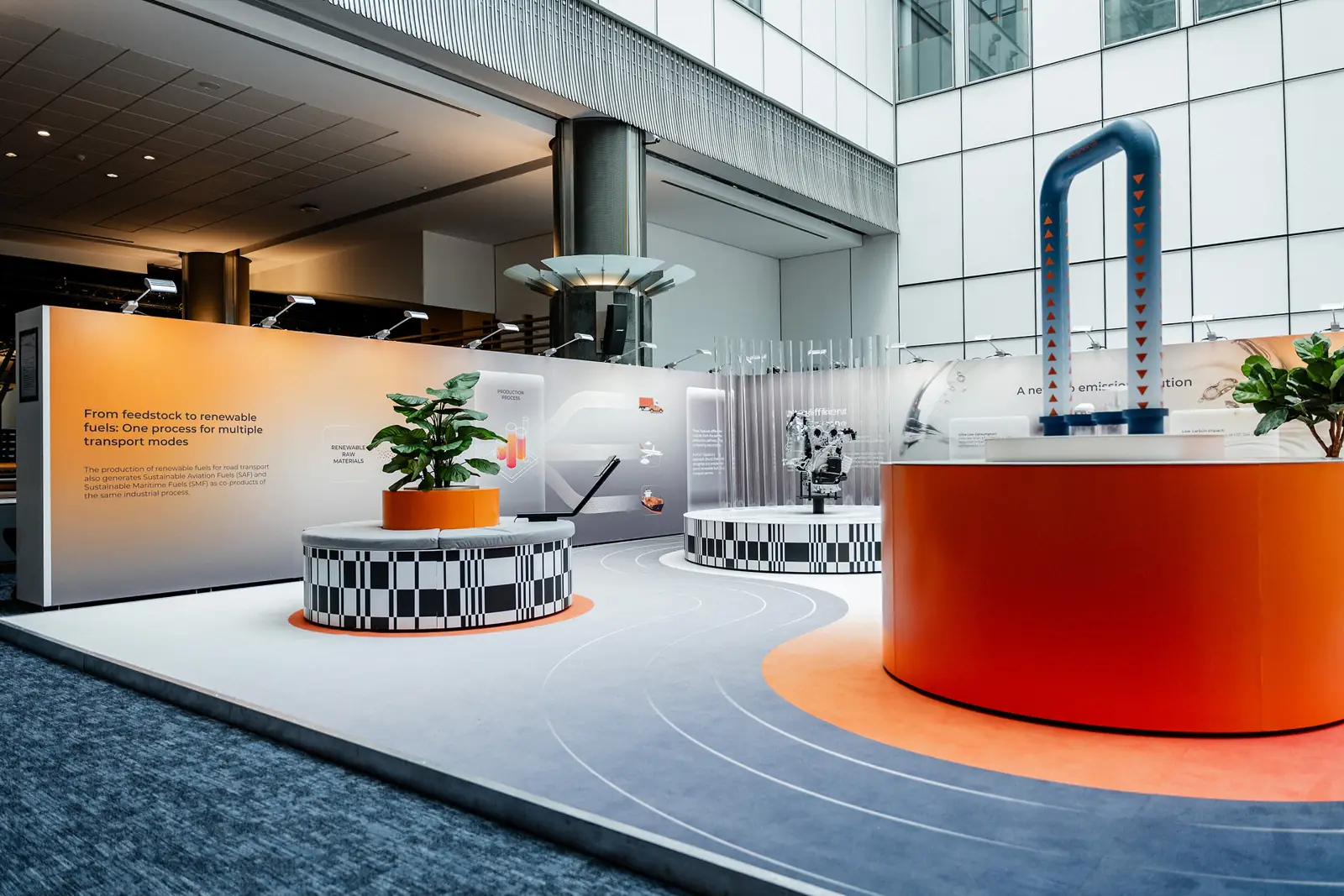 The stand seen across the hall: an orange plinth, the engine on a chequered stand and a wall reading &ldquo;From feedstock to renewable fuels&rdquo;