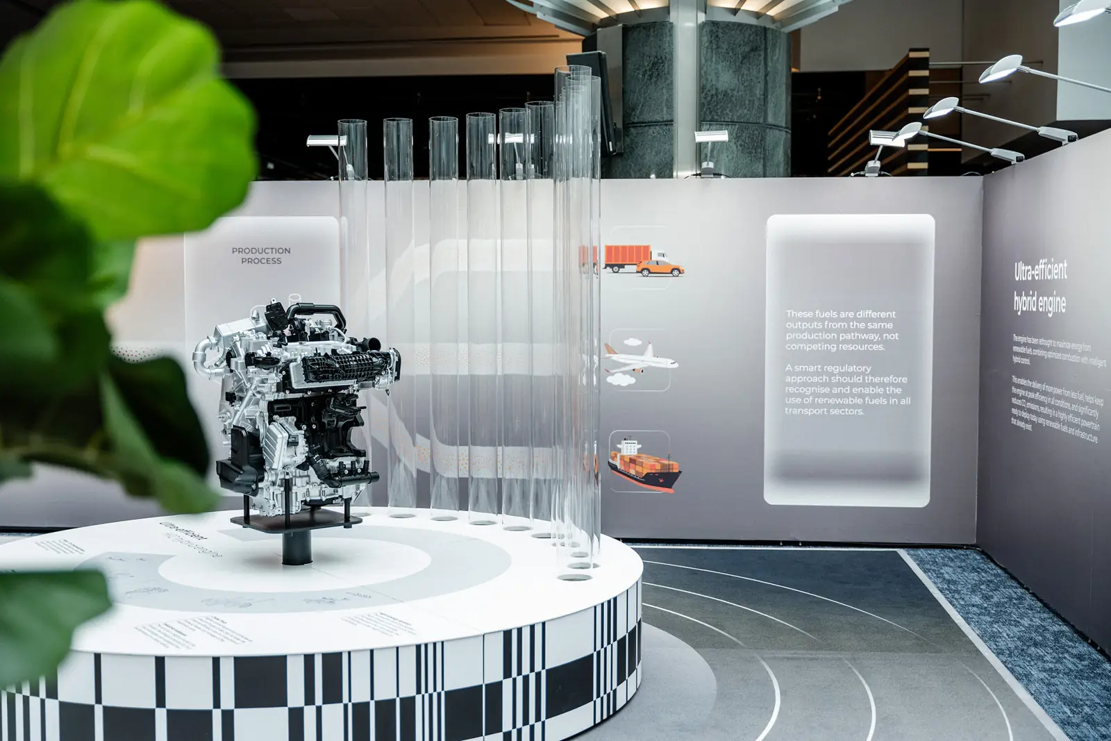 The hybrid engine on a chequered plinth in front of a wall explaining the fuel production process
