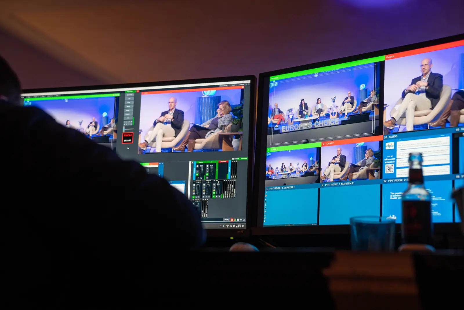 The AV control desk, with live camera feeds on the monitors