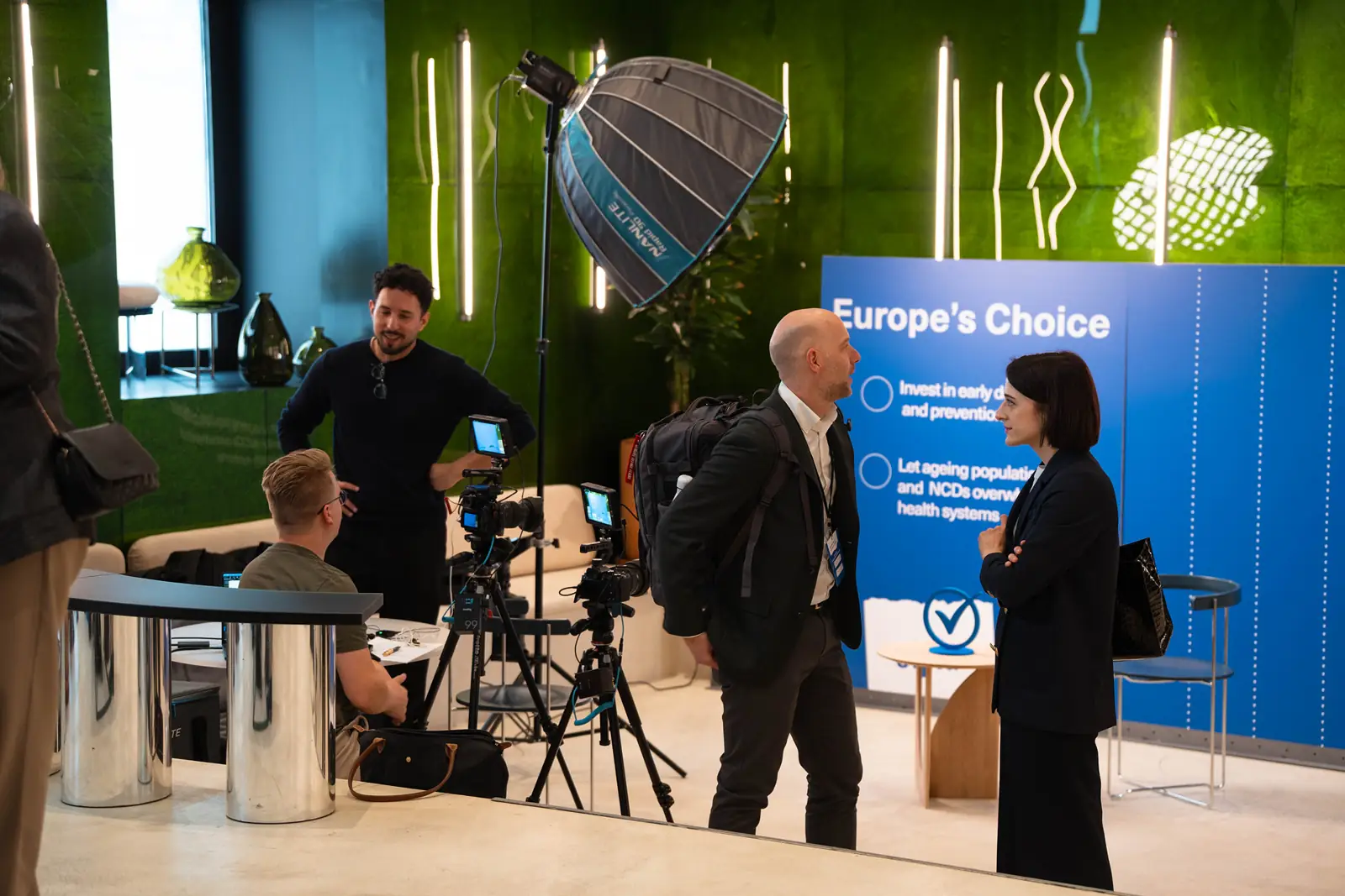 Speakers preparing on the interview set while the crew sets up cameras